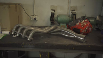 racecraft merge collector on a custom header on a fabrication bench next to welding helmet