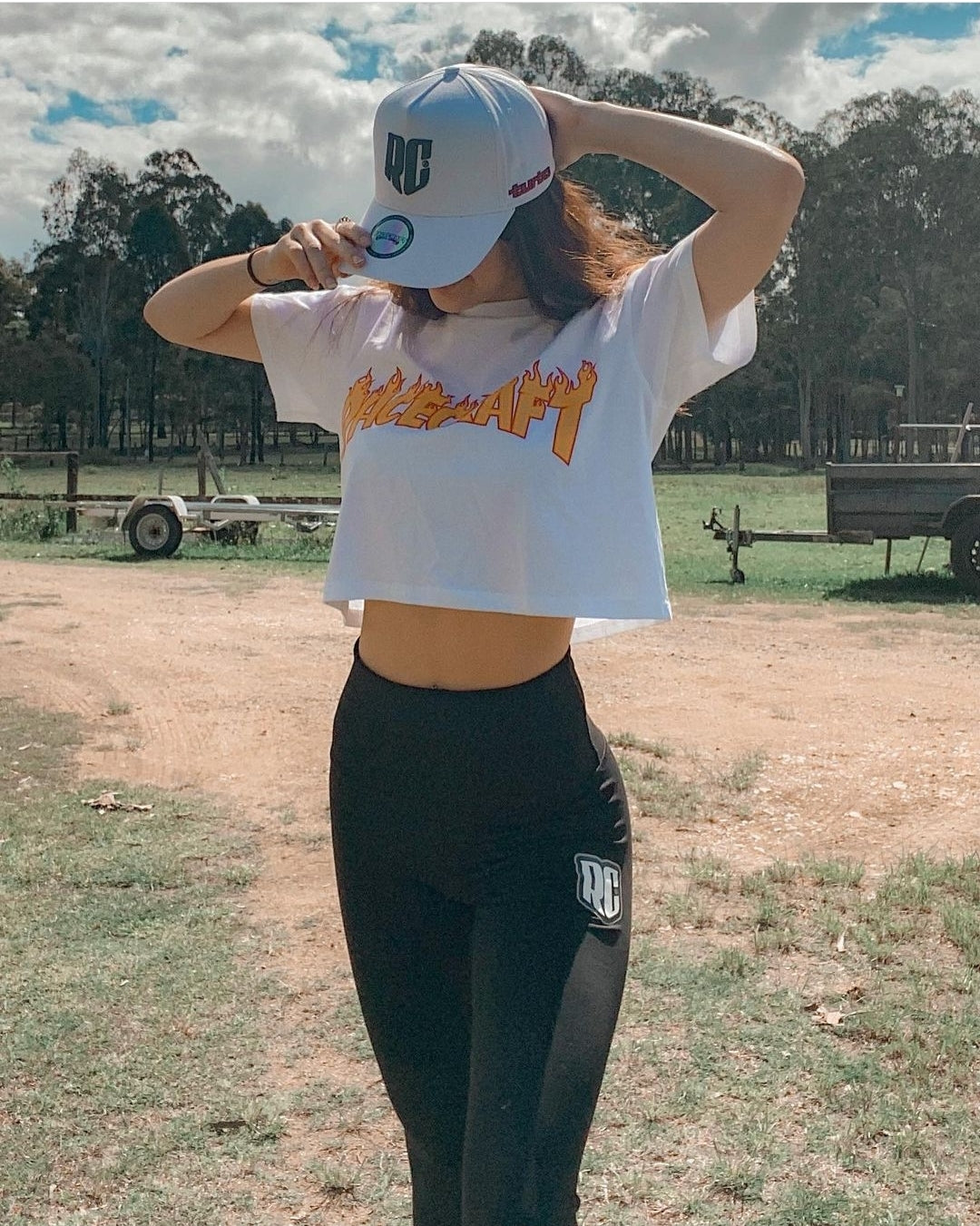 Lifestyle shot of Girl wearing a white Racecraft crop top with orange text and black RC apparel leggings outdoors.