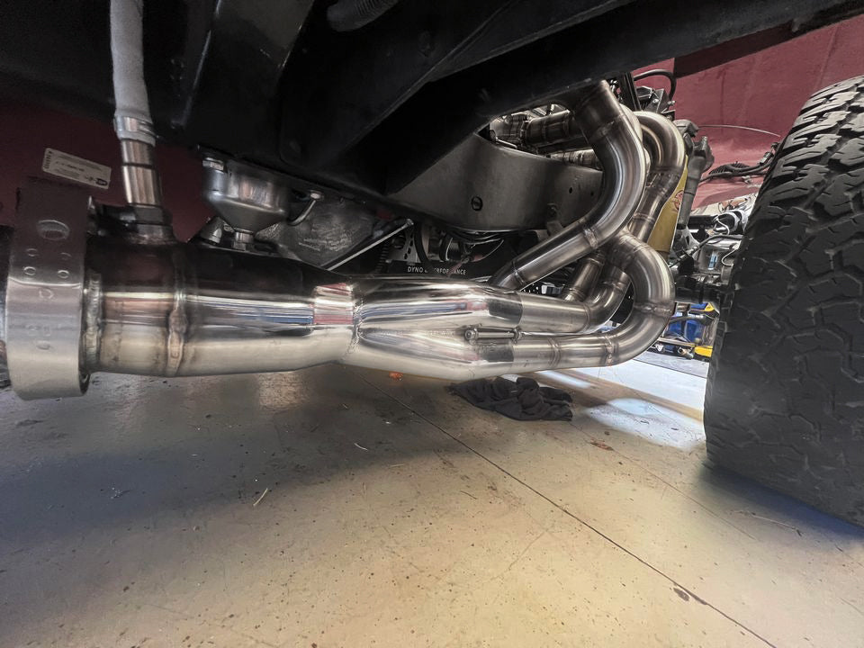 Close-up of a vehicle's exhaust system with a focus on the racecraft 4 into 1 merge collector on custom header