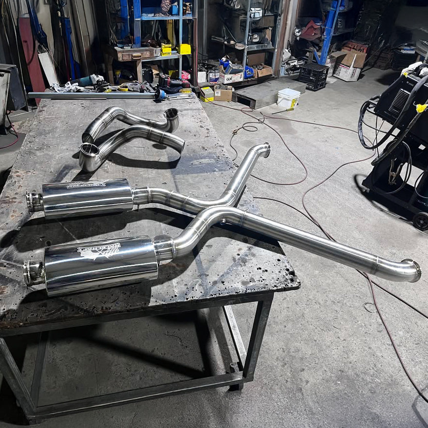 fabricated custom stainless racecraft exhaust pipes on a workbench in a workshop setting