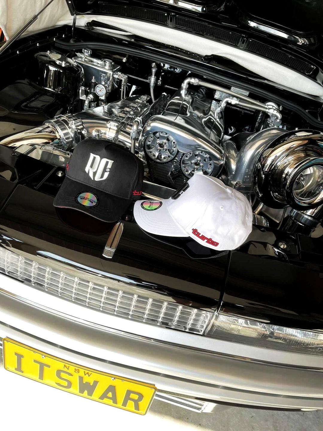 black vl turbo a-frame snapback cap and white vl turbo a-frame snapback cap in the engine bay of a holden commodore vl turbo with large turbo